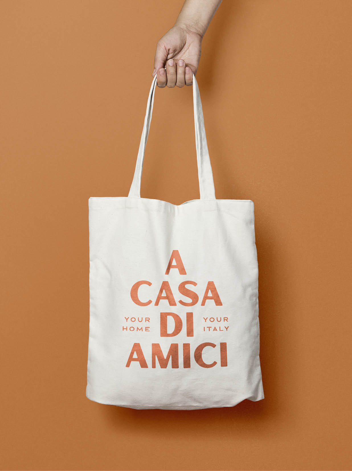 Weiße Stofftasche mit Logo „A CASA DI AMICI“ in Rot und Grün auf orangefarbenem Hintergrund.