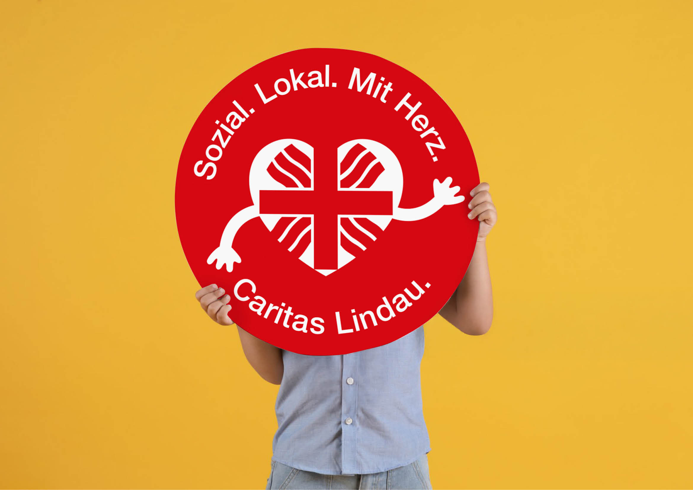 Hand hält Schild mit Logo Caritas Lindau und Aufdruck „sozial. Lokal. Mit Herz.“