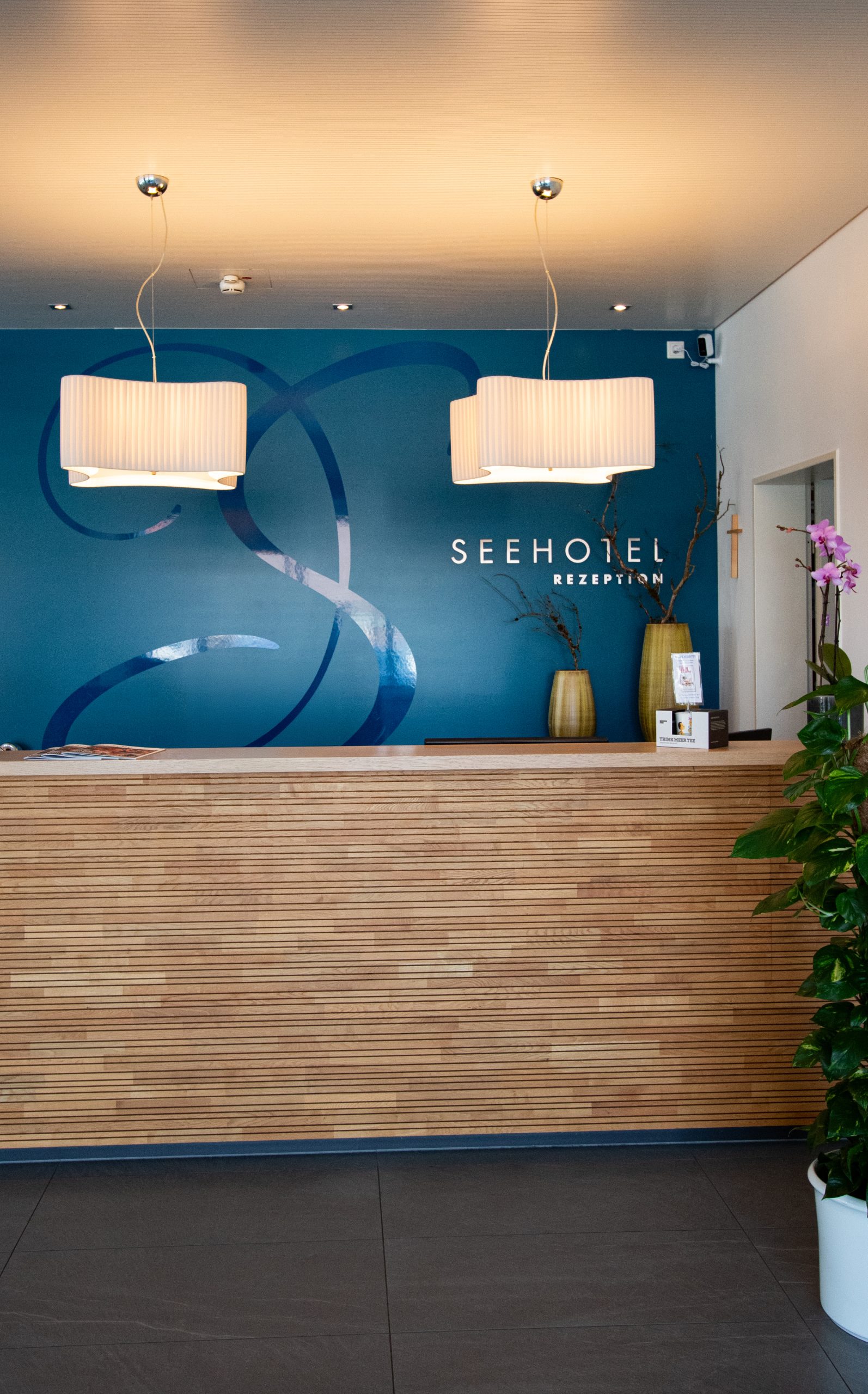 Rezeption mit Holztresen, blauer Wand und Schild „Seehotel Rezeption“