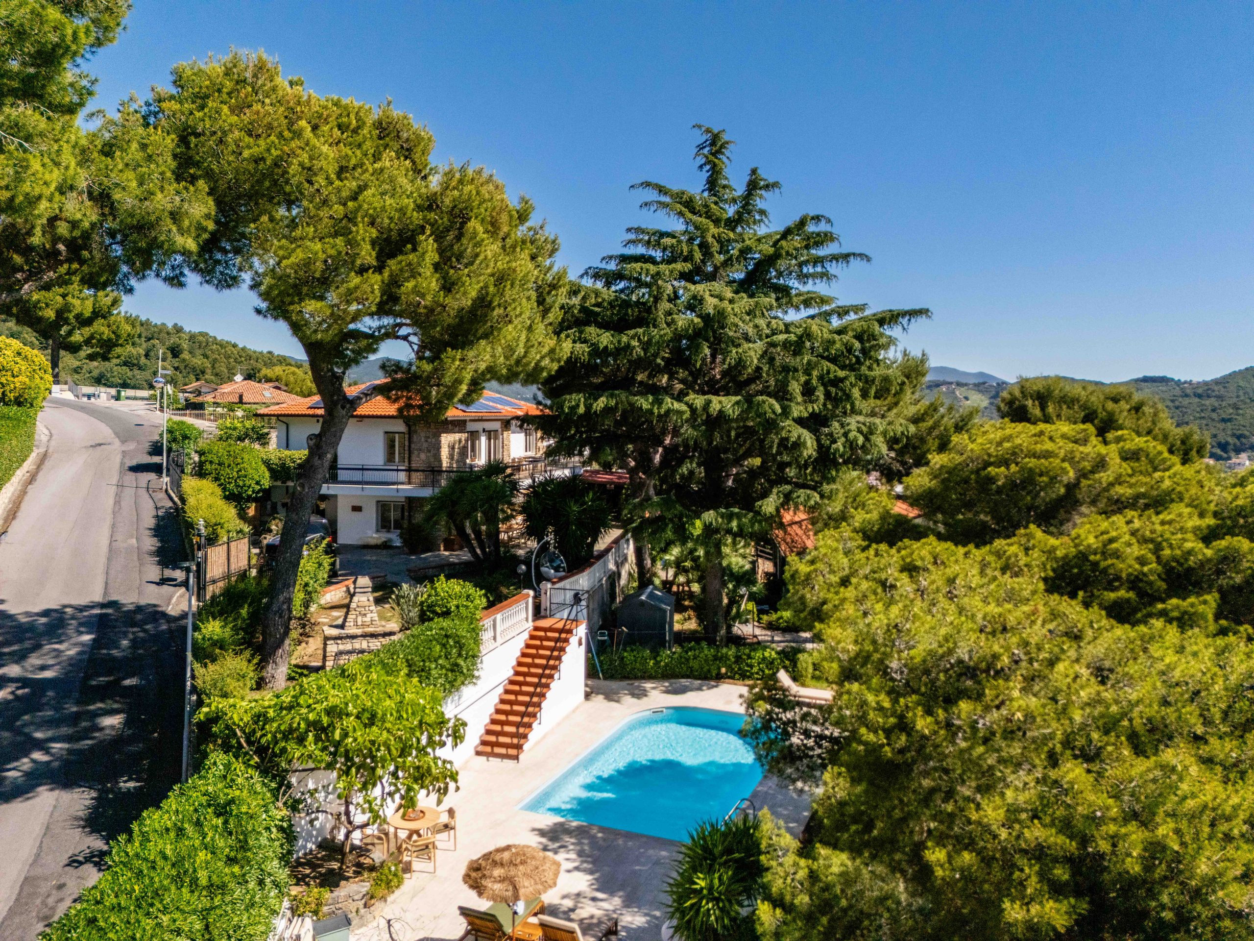 Villa mit Pool, Treppe und Terrasse umgeben von üppiger Vegetation und Bergen im Hintergrund