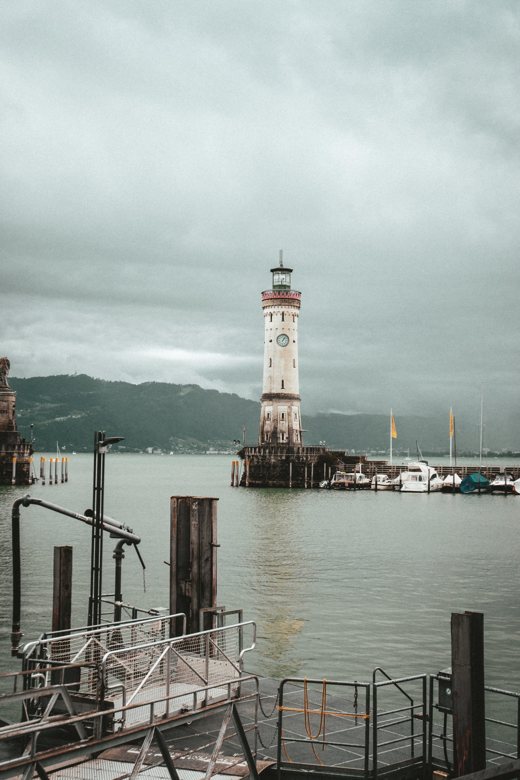 Steg mit Leuchtturm am Seeufer bei bewölktem Himmel